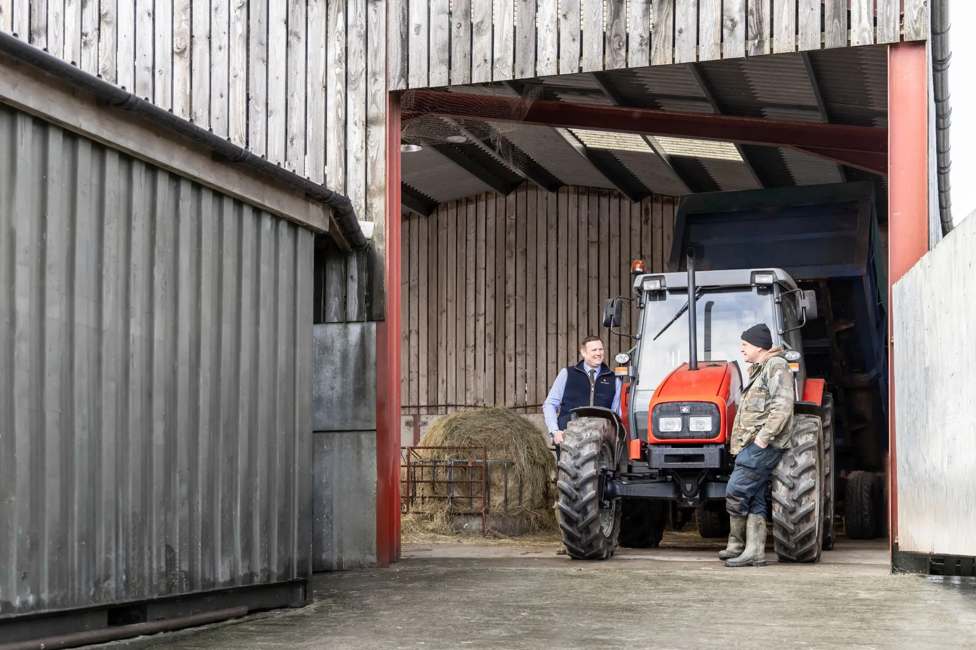 Farm consultant and client talking near red tractor