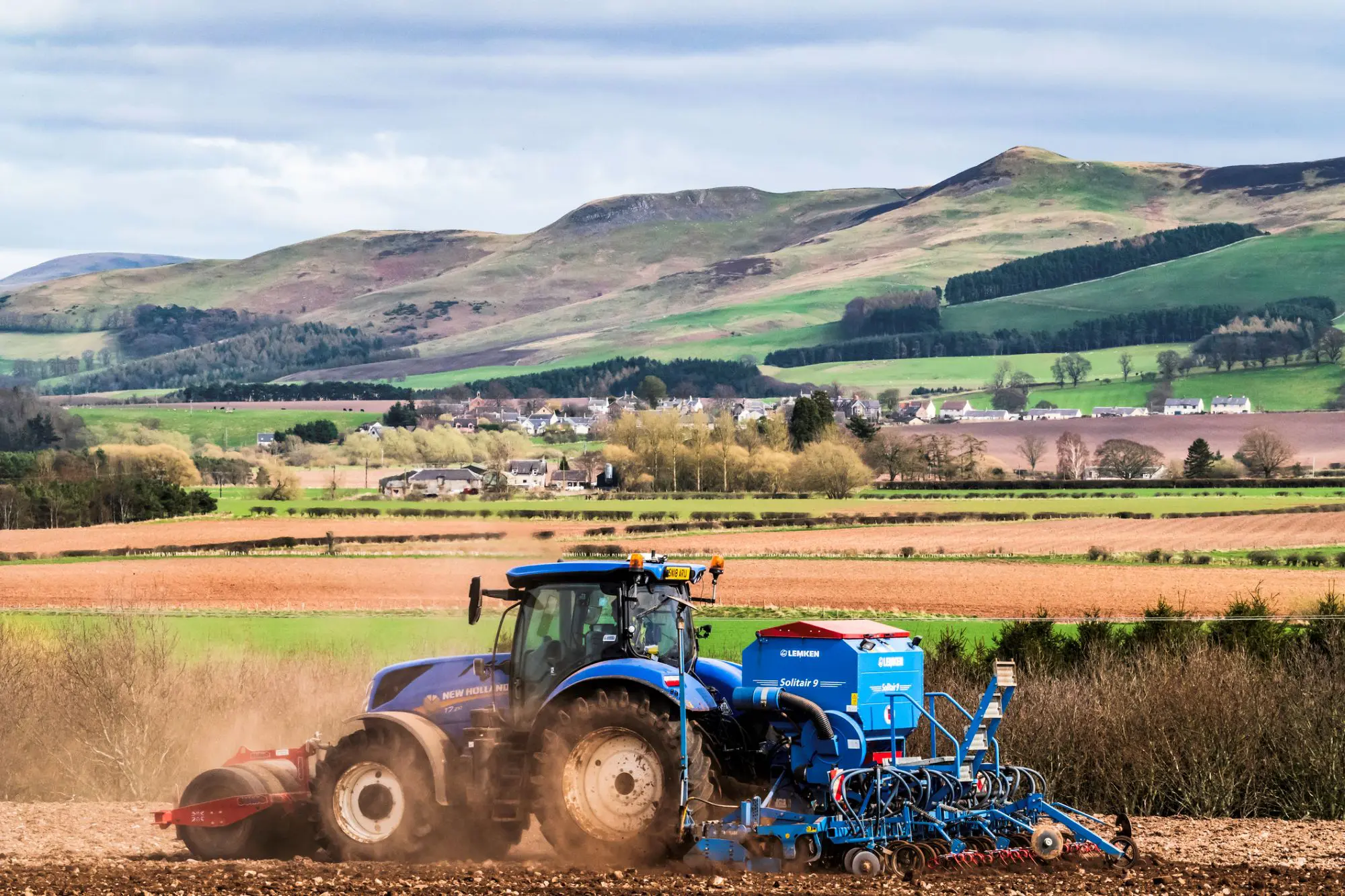 Blue tractor with blue seed drill planting crops