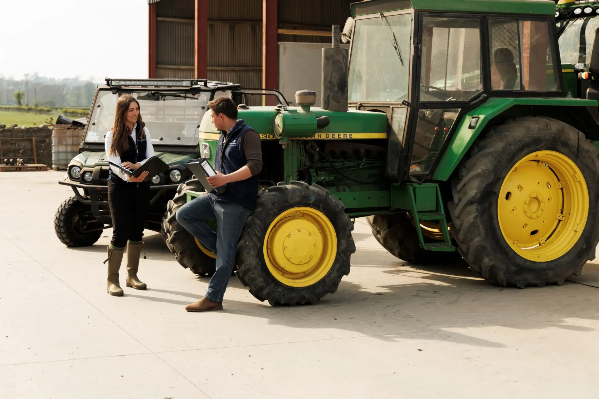 Farm consultant talking to client with tractor and ATV in background